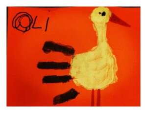 Praca dziecka ptak: na czerwonej kartce odciśnięty żółty ślad rączki dziecka i domalowane do tego elementy: ogon, dziób, oko.