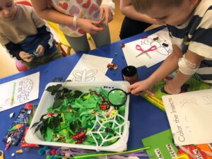 na stole kuweta, w której znajdują się prace dzieci: ręcznie robione liście, rośliny i owady