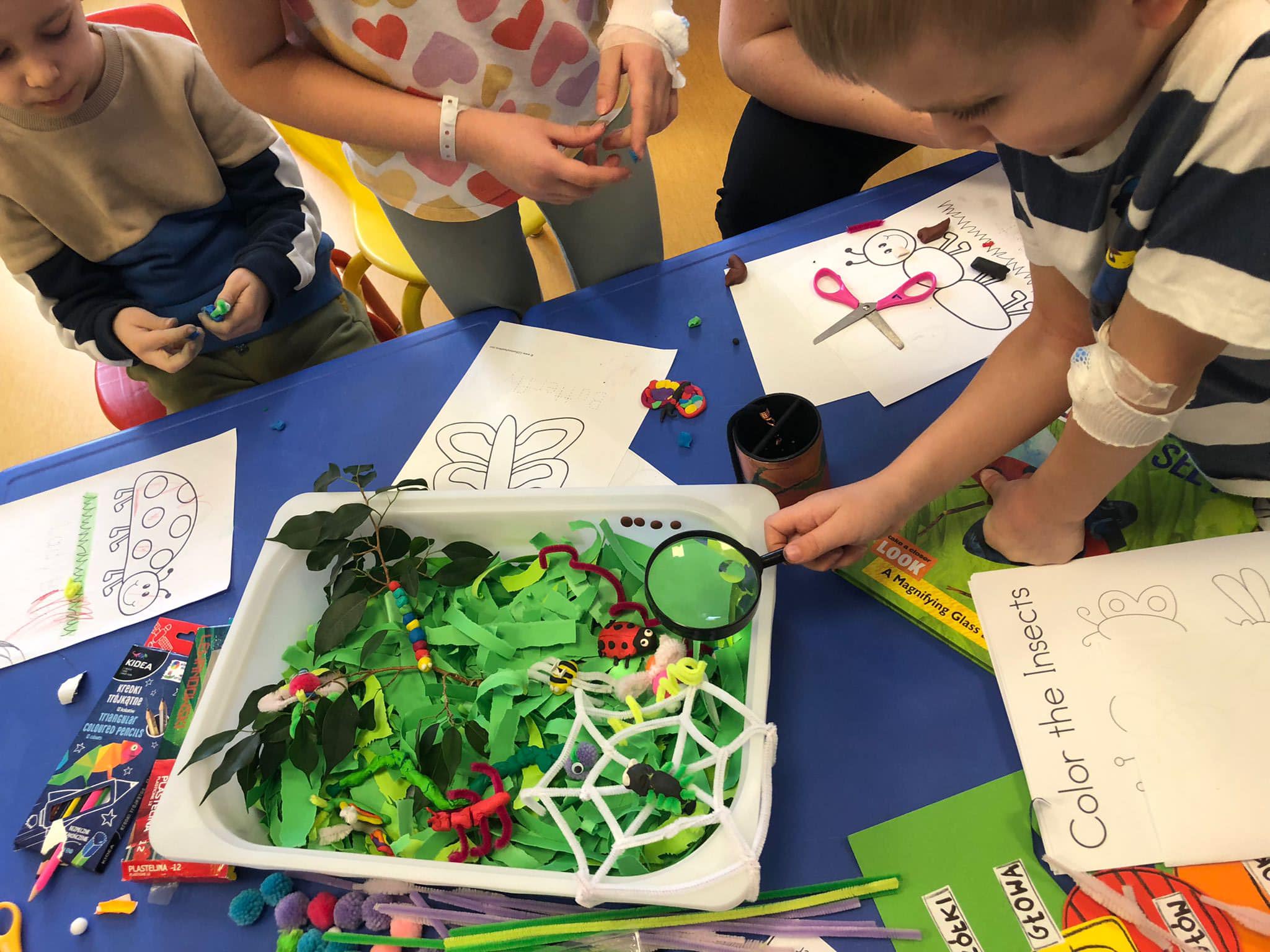 na stole kuweta, w której znajdują się prace dzieci: ręcznie robione liście, rośliny i owady