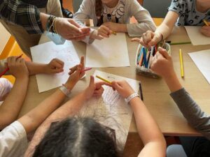 dzieci siedzą dookoła stołu. na stole karty pracy. dzieci mają wyciągnięte rączki i bawią się paluszkami