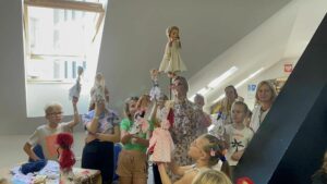 dookoła pani stoją dzieci. wszyscy mają podniesione do góry własnoręcznie wykonane lalki - kukiełki