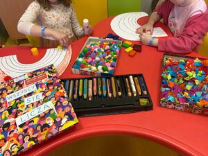 stolik, na którym dzieci wykonują prace plastyczne obrazujące tęczę używając kredek i pomponików