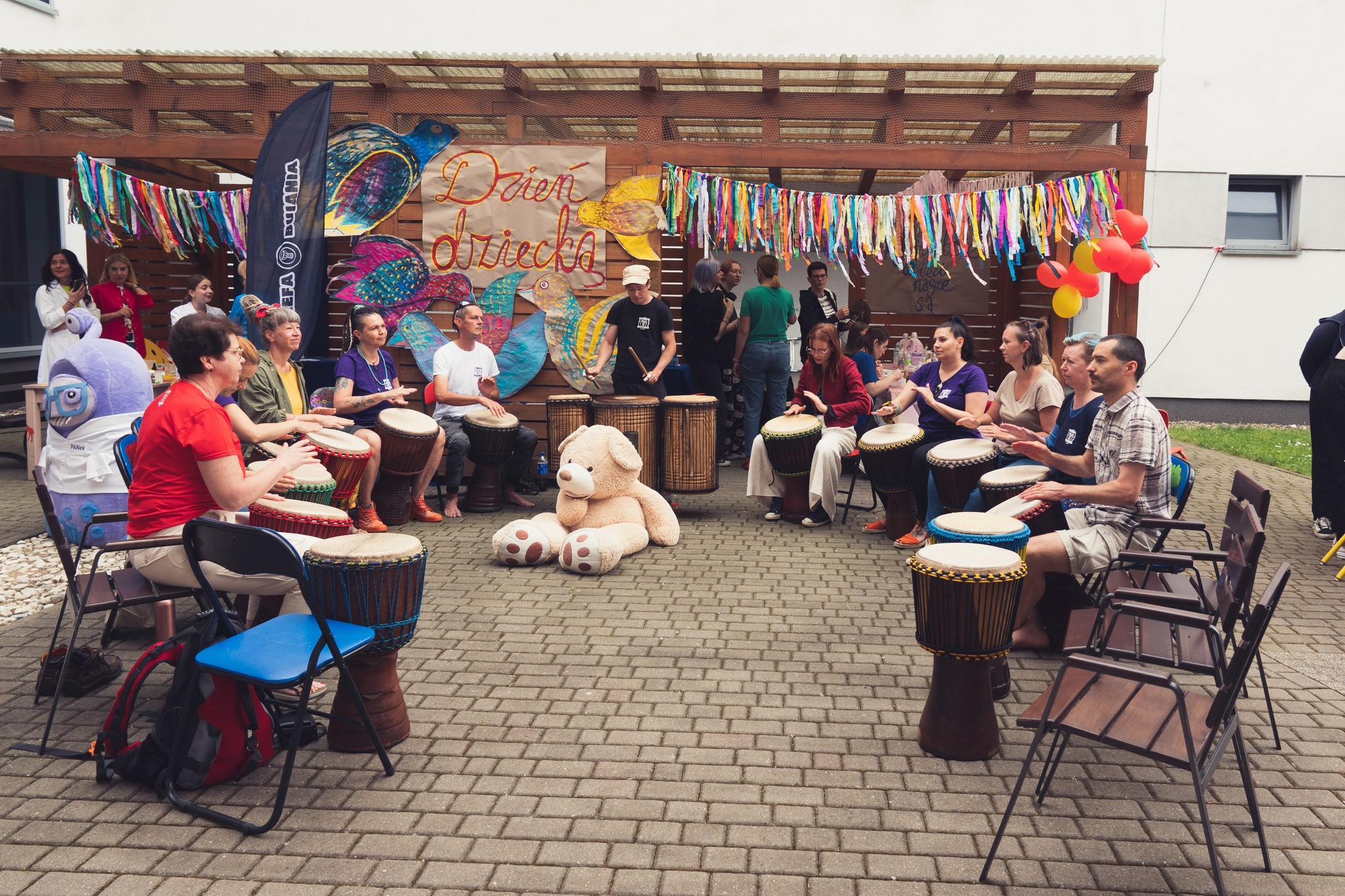 grupa bębniarzy gra na patio szpitalnym, w tle plakat z napisem dzień dziecka