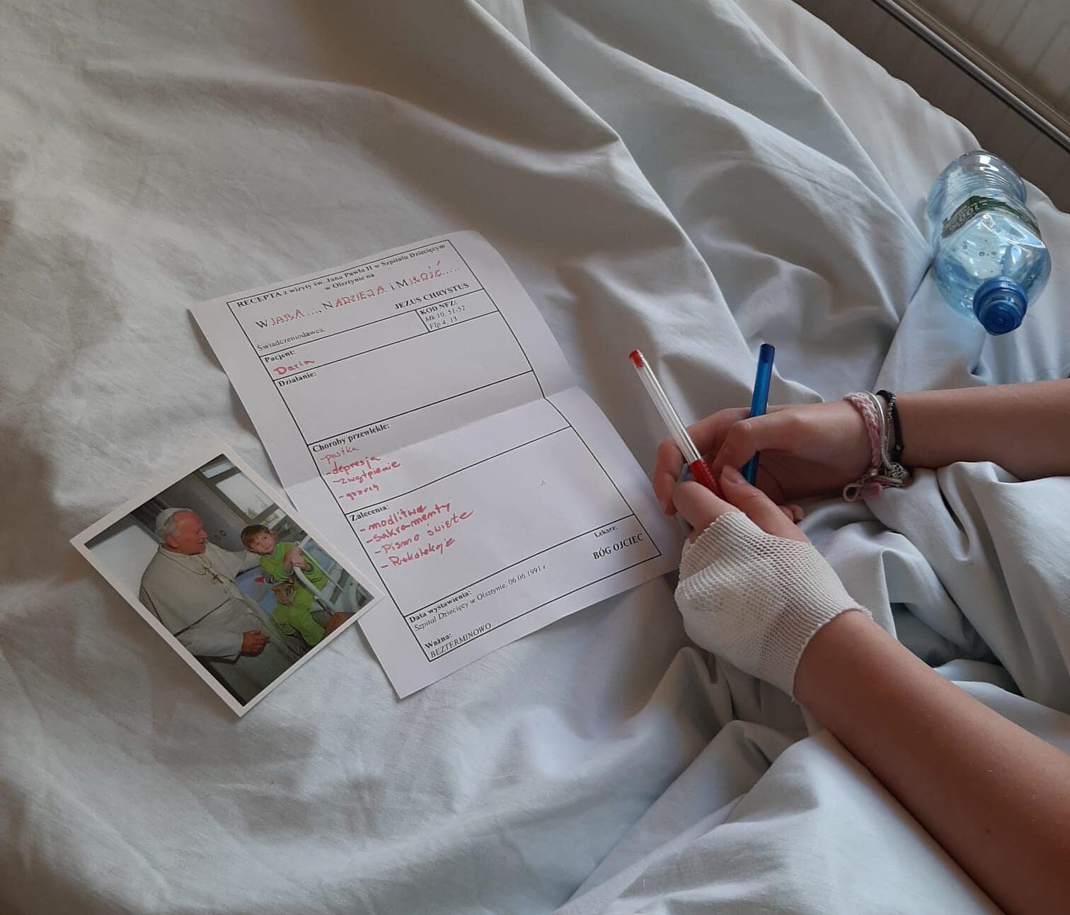 dziecko siedzace na lozku szpitalnym wypelnia karte pracy o janie pawle 2