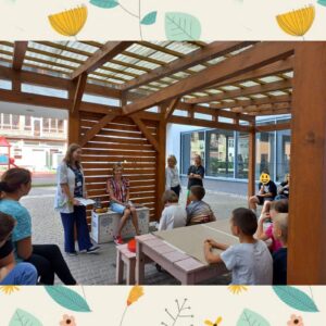 dzieci siedzą na patio szpitalnym, słuchają nauczycielki