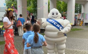 Ludzik Michelin wita dzieci na patio, obok stoi nauczycielka